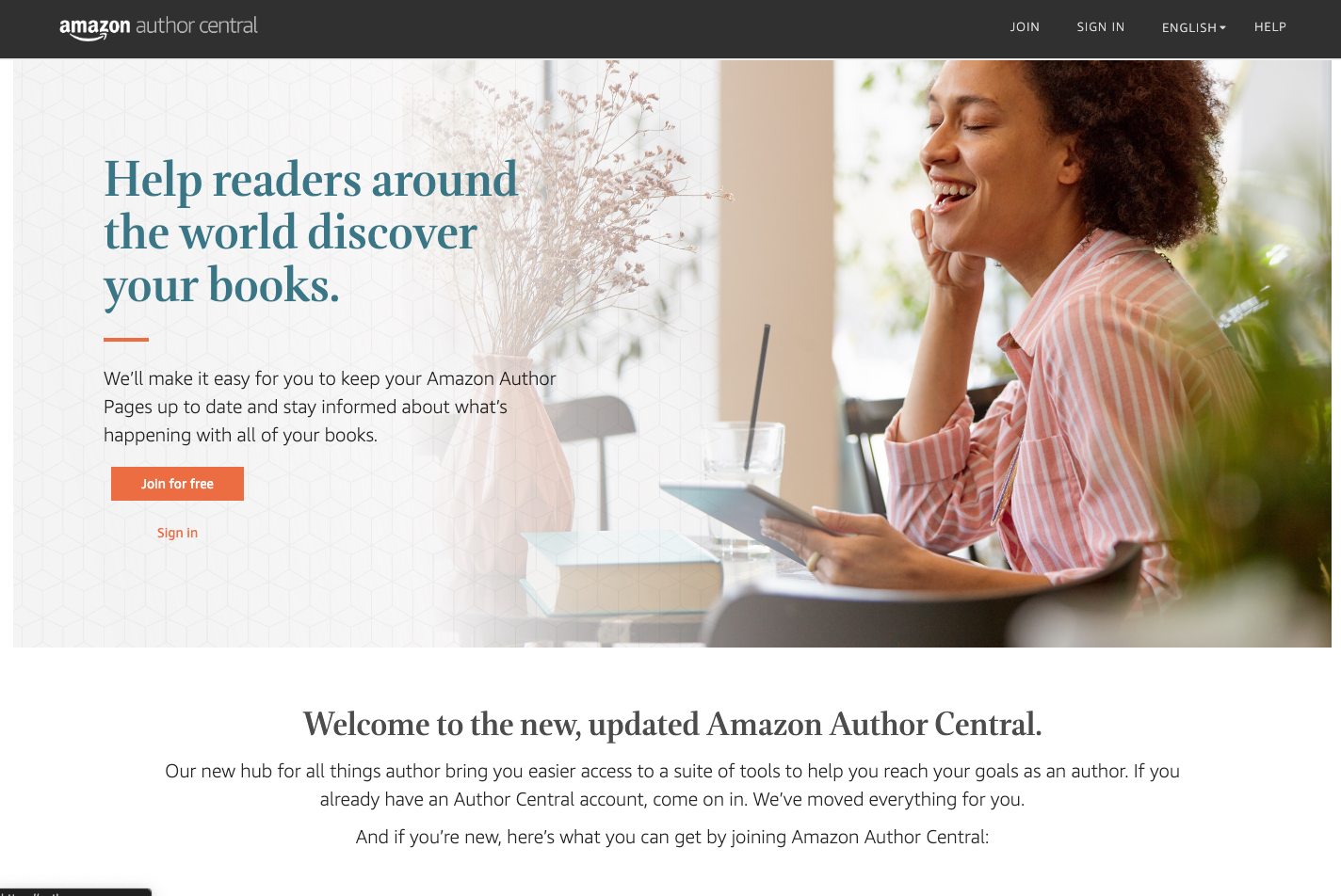 Woman in pink striped shirt smiling while holding tablet near window with plants and books